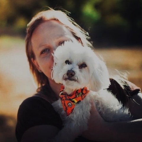 Dori holding a small white dog in an orange bandana
